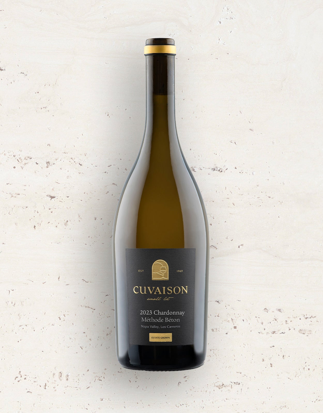 A bottle of 2024 Cuvaison Chardonnay, Méthode Béton stands upright against a pale, textured background, featuring a black label with gold and white text and a small gold emblem.
