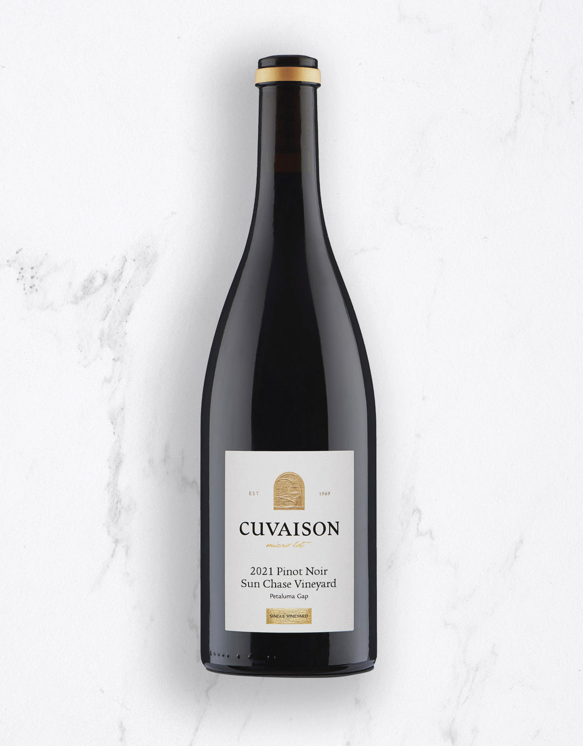 A bottle of Cuvaison 2021 Pinot Noir from the San Chasis Vineyard, photographed from a top-down angle on a white marble background.