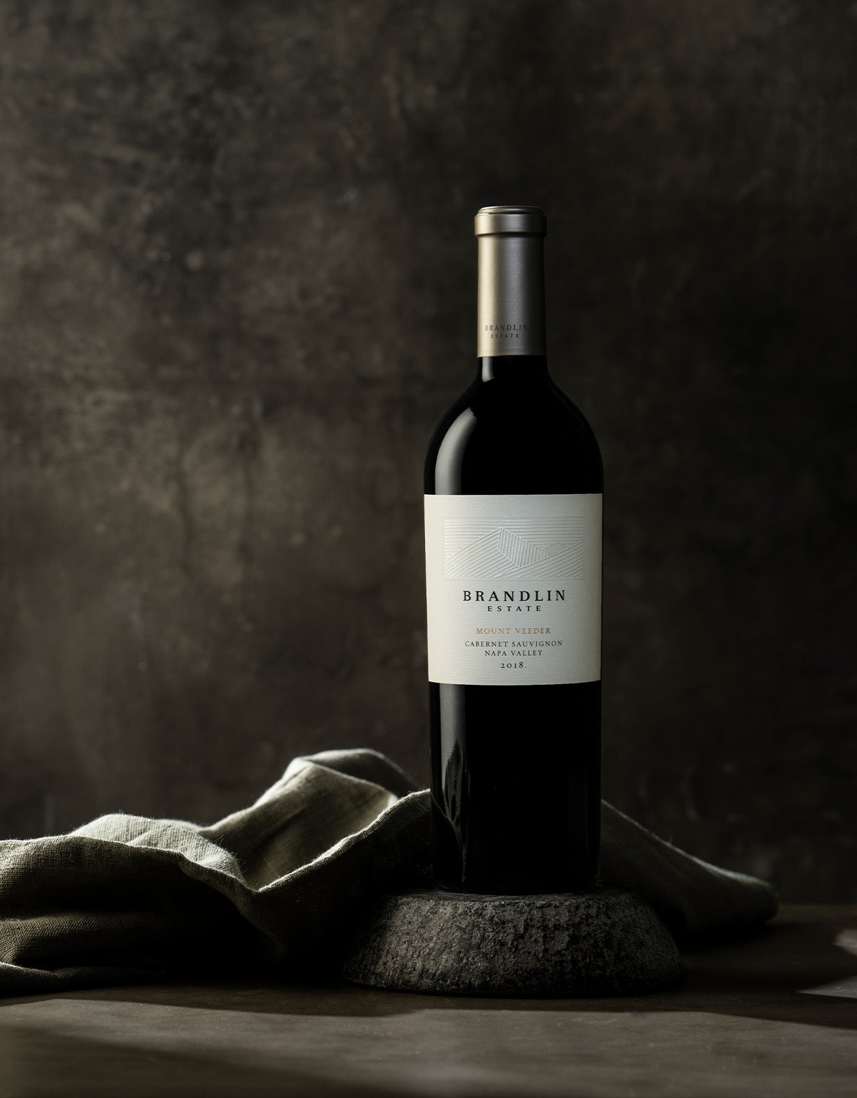 A Brandlin Estate Cabernet Tasting Kit rests on a stone slab with a folded gray cloth beside it, set against a dark, textured background.