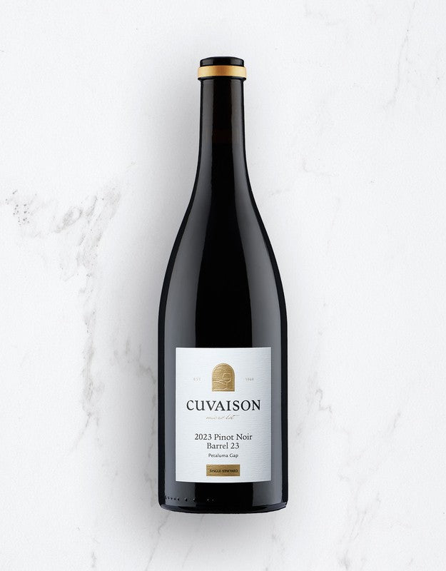 A bottle of 2023 Cuvaison Barrel 23 Pinot Noir stands upright on a white marble surface, showcasing a gold and white label with black text and a gold foil seal on the neck.