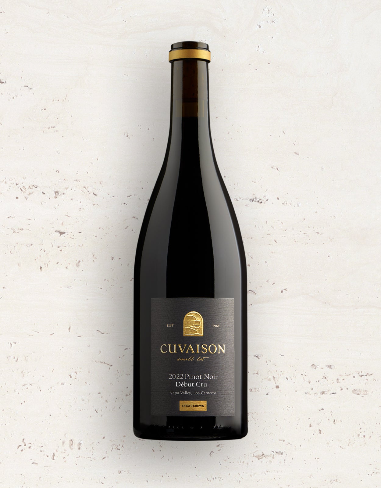 A dark glass bottle of 2022 Cuvaison Pinot Noir, Debut Cru stands upright on a light-colored, textured surface. The bottle displays a black and gold label with the vineyards branding and vintage details.