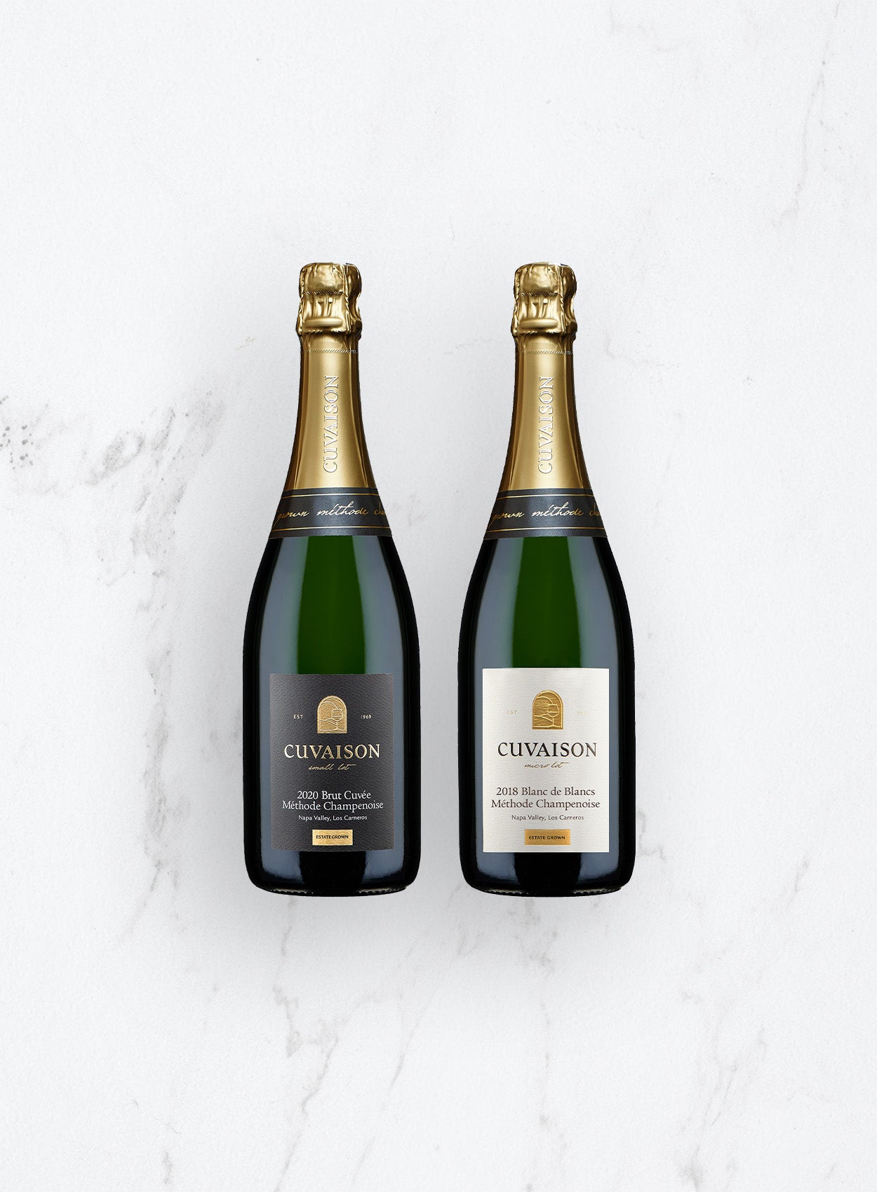 Two bottles from the Cuvaison Sparkling Duo, one with a dark label and one with a light label, both topped with gold foil, are placed side by side on a white marble surface.