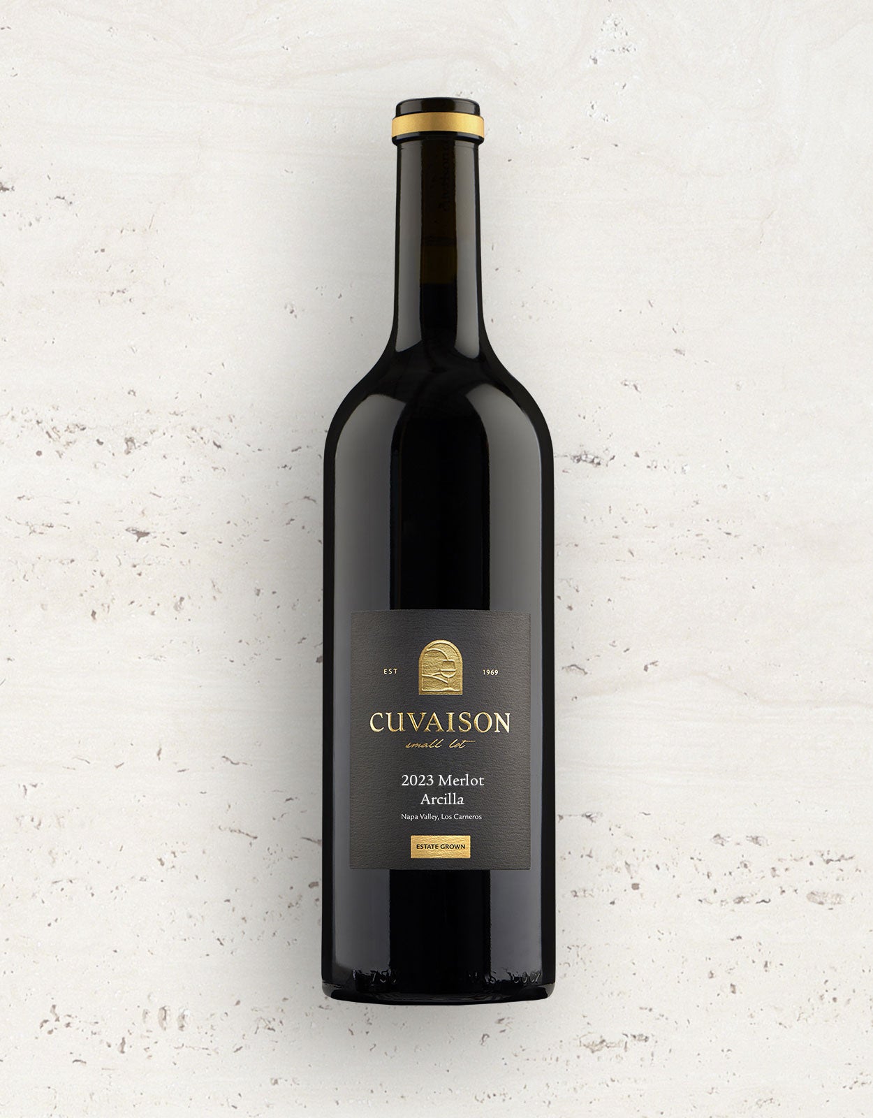 A bottle of 2023 Cuvaison Merlot, Arcilla with a black label and gold text stands upright on a light, textured surface.