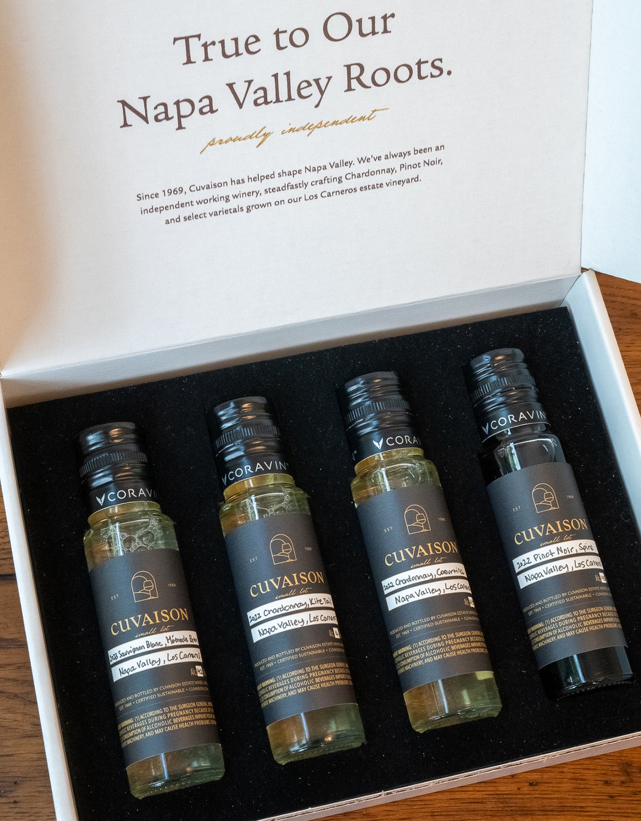 An open box of the Cuvaison The Small Lot Tasting Kit displays four small wine bottles in black foam. The lid describes Napa Valley roots and Cuvaison’s history, with each bottle labeled by varietal and vintage.