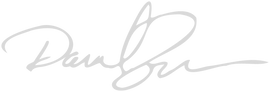 A stylized, cursive signature written in light gray ink on a plain, light background. The signature consists of large loops and flowing lines.