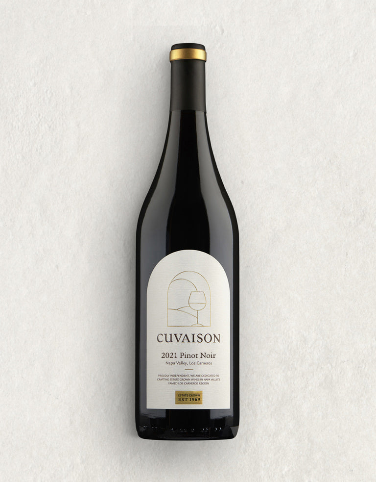 A bottle of Cuvaison 2021 Pinot Noir wine stands upright on a light, textured surface. The label is white with gold and black text, featuring a minimalist line drawing of a wine glass.