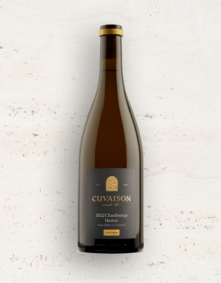A bottle of 2023 Cuvaison Chardonnay, Hedon with a black label featuring gold text and a gold logo, set against a light, textured background.