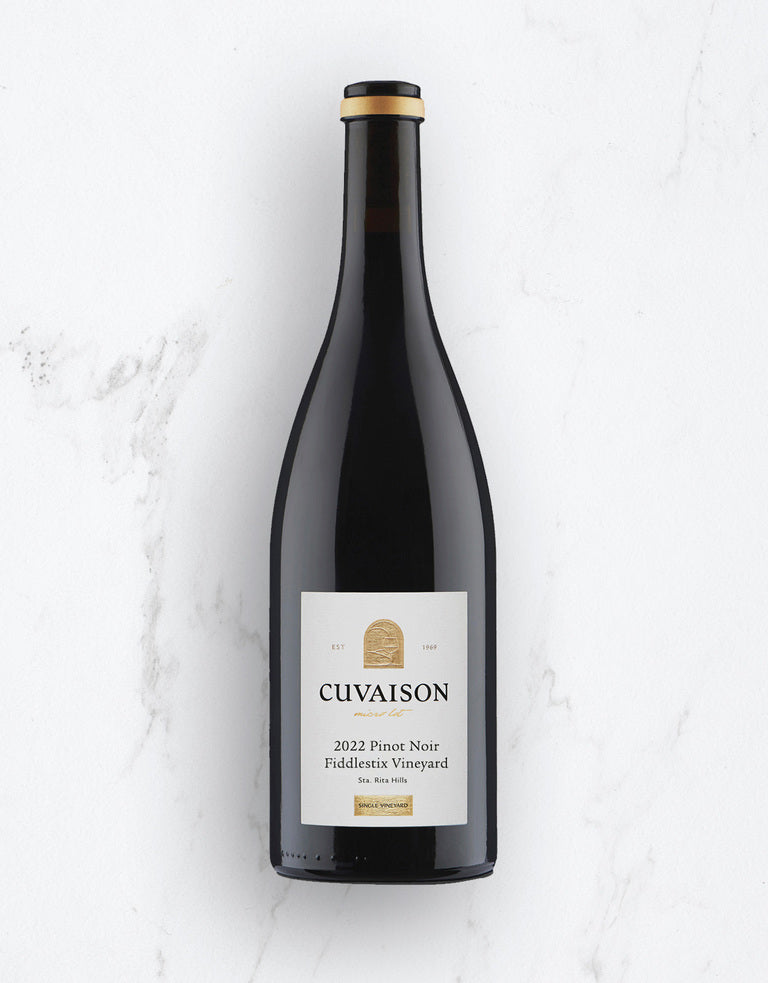 The 2022 Cuvaison Pinot Noir, Fiddlestix Vineyard, featuring a white and gold label, is shown upright on a white marble surface.