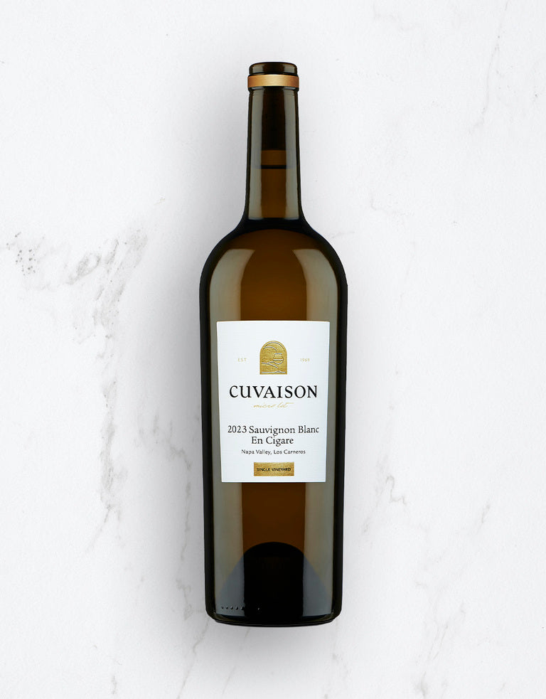 A bottle of 2023 Cuvaison Sauvignon Blanc, En Cigare stands upright on a white marble surface, featuring a label with gold and black text and a circular gold emblem at the top.