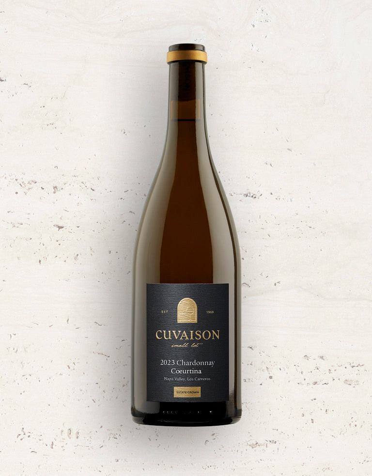 A bottle of 2023 Cuvaison Chardonnay, Coeurtina stands upright against a light, textured background. Its dark label showcases the brand name, vintage, and wine details in gold and white text.