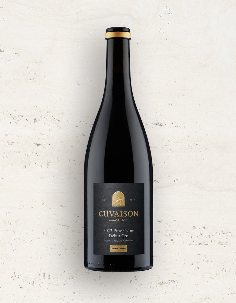 A bottle of 2023 Cuvaison Pinot Noir, Début Cru stands upright against a light, textured background, displaying its black and gold label with the vineyard’s logo and text.
