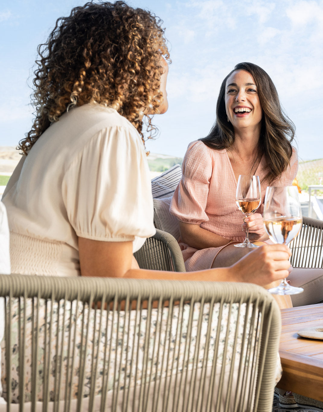 Two women sitting at a table outdoors, enjoying glasses of wine.